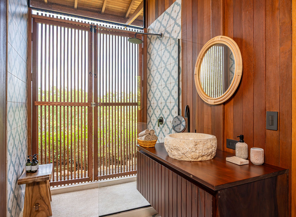 Bedroom one bathroom with stone vessel basin, rattan mirror and louvered shower doors