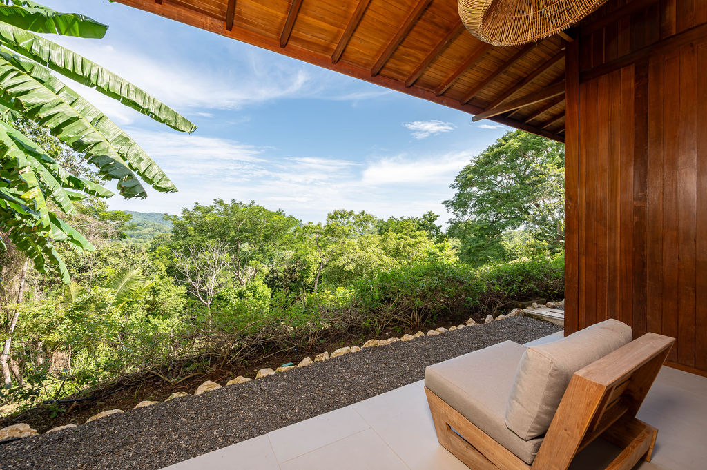 Bedroom two terrace corner chair framed by banana leaves and open sky