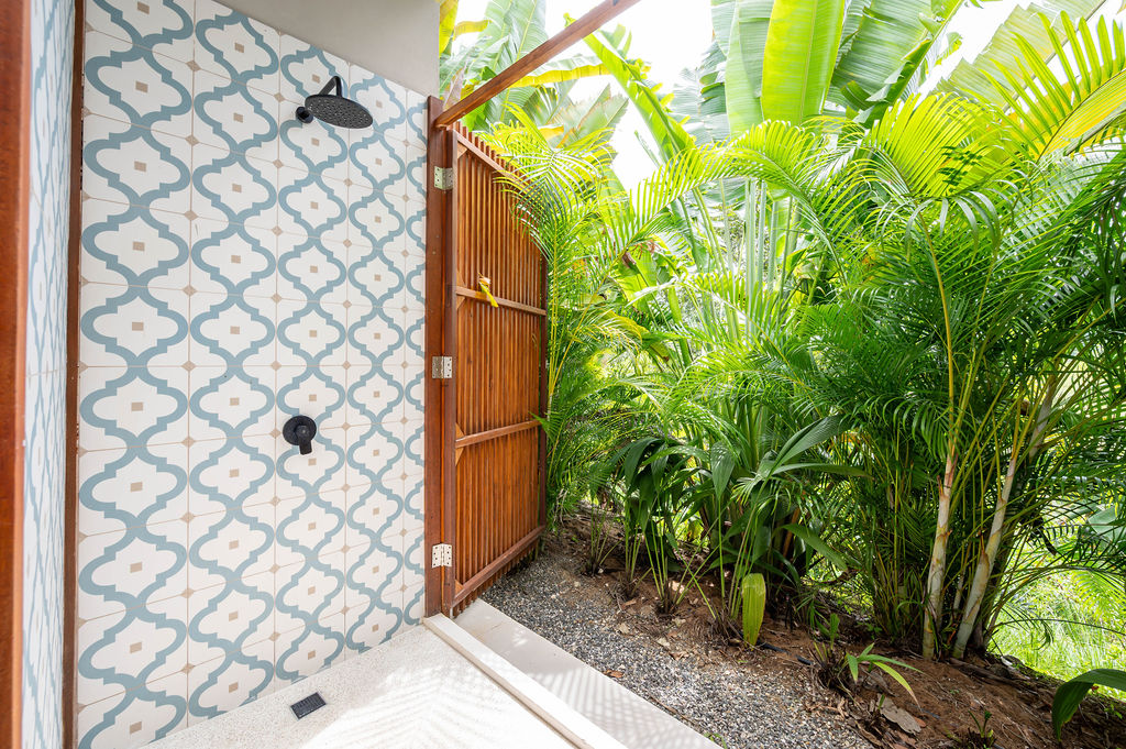 Outdoor shower clad in blue and white patterned tile, surrounded by foliage